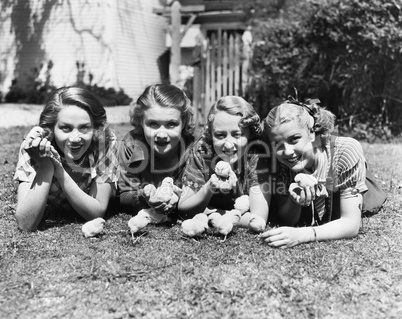 Four young women lying outside with baby chicks.