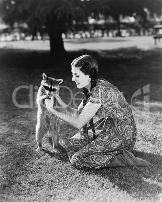 Woman kneeling on the lawn playing with a tame raccoon