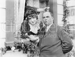 Man having his hair pulled by a hand coming out of a window while standing next to a woman