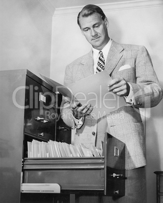 Businessman looking at a paper next to a filing cabinet