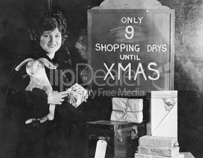 Woman with gifts and sign with number of shopping days until Christmas