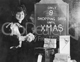 Woman with gifts and sign with number of shopping days until Christmas