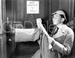 Man leaning against a door with his legs up and reading a newspaper