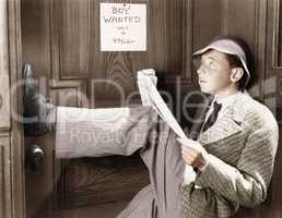 Man leaning against a door with his legs up and reading a newspaper