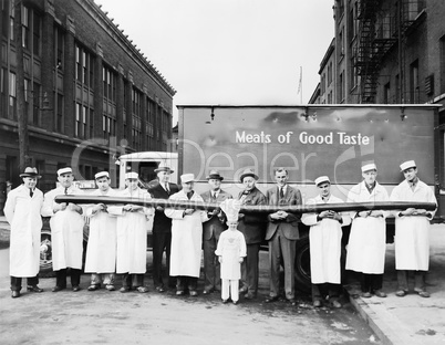 Butchers showing off a long sausage in front of a truck