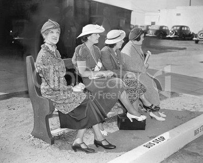 Four women sitting on a bench waiting for the bus