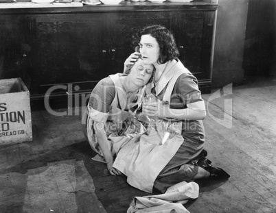 Two women sitting on the floor while one is holding the other