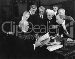 Men hovering around desk in anticipation of news