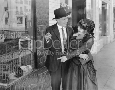 Young woman with man pointing at cats in cage for sale