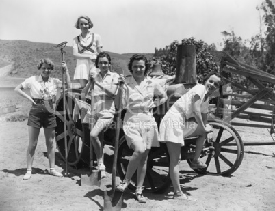 Young women with gardening tools standing near wooden cart