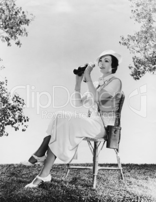 Elegant woman sitting on chair while holding binoculars