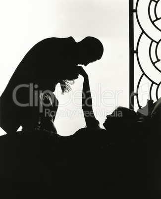 Silhouette of man kissing reclining woman's hand