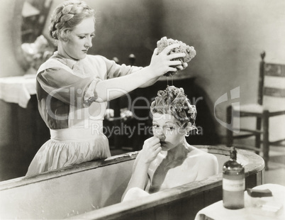Maid squeezing sponge on woman in bathtub