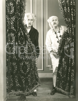 Two men spying from behind drapes