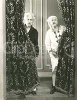 Two men spying from behind drapes
