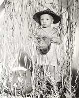 Little boy in Halloween costume holding mask standing by streamers