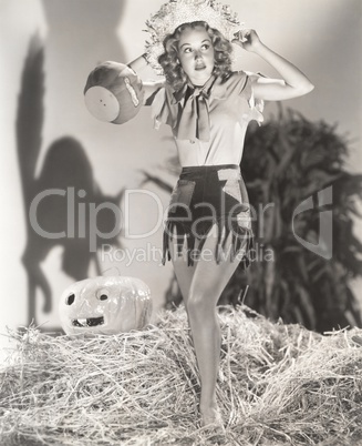 Young woman standing on haystack in front of shadow of cat on wall