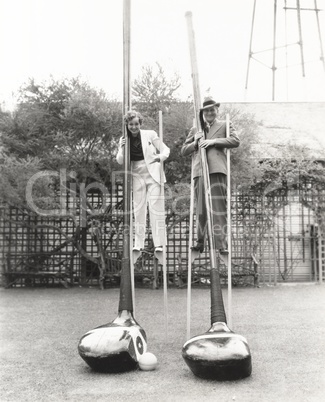 Man and woman on stilts holding giant golf clubs