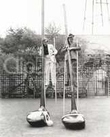 Man and woman on stilts holding giant golf clubs