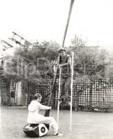 Man on stilts holding onto giant golf club with woman seated on it