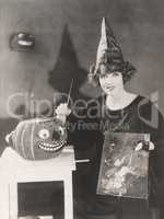 Woman in pointy hat painting a jack o'lantern