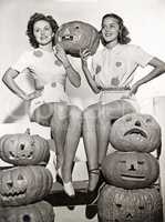 Two women sitting on fence with carved pumpkins