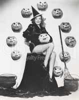 Bewitching woman sitting among carved pumpkins