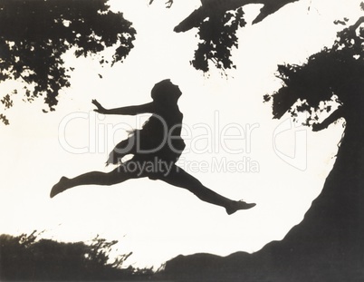 Silhouette of a woman in mid-air jumping between two trees