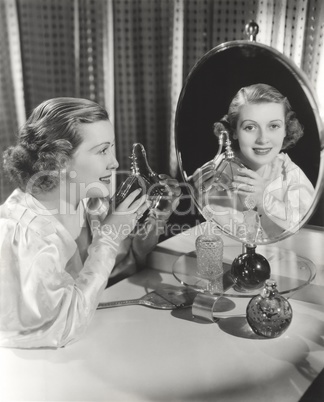 Reflection of woman holding perfume atomizer in mirror