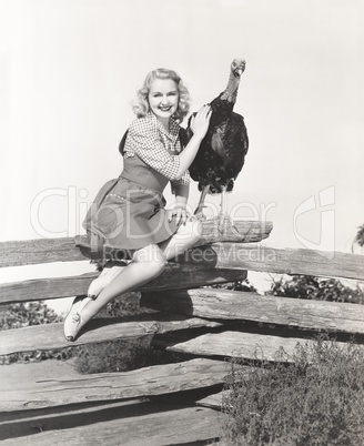 Woman sitting on fence petting her turkey