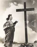 Woman singing hymns by a large wooden cross on a hill