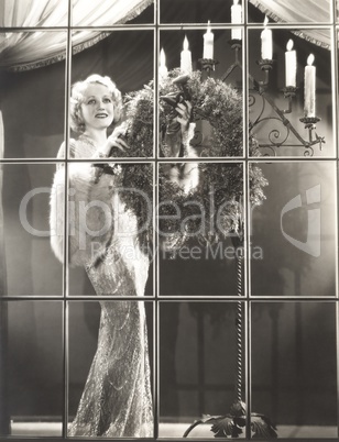 Woman in evening gown putting Christmas wreath in window