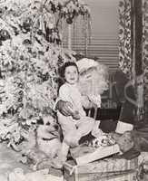 Little girl sitting on Santa's lap under Christmas tree