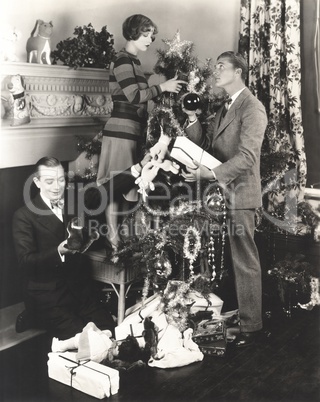 Men helping woman decorate Christmas tree at home