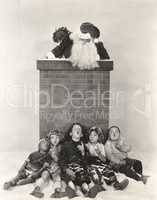 Children sitting against chimney looking at Santa Claus