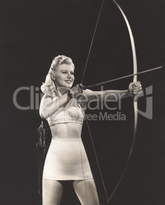 Woman in crop top and mini skirt shooting bow and arrow