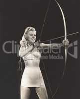Woman in crop top and mini skirt shooting bow and arrow