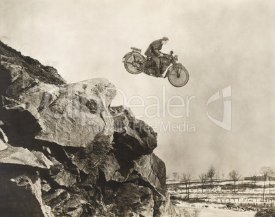 Stuntman on motorbike flying over cliff