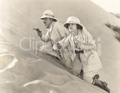 Armed couple climbing up sand dune