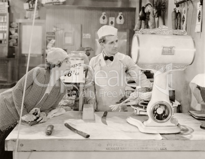 Butcher and customer looking at weight of chicken on scale