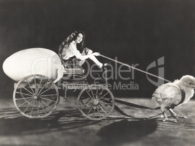 Baby chick pulling cart with woman and giant egg