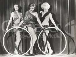 Three scantily clad women holding large rings