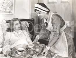 Maid serving breakfast to woman lying in bed