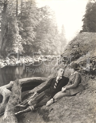 Couple sitting on rock beside stream