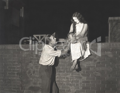 Man wooing woman sitting on brick wall