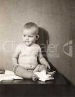 Chubby baby boy sitting on table with diaper off