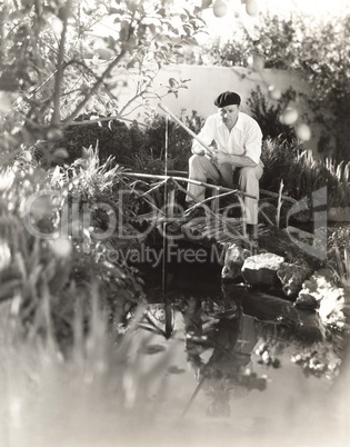 Man sitting on footbridge fishing in pond