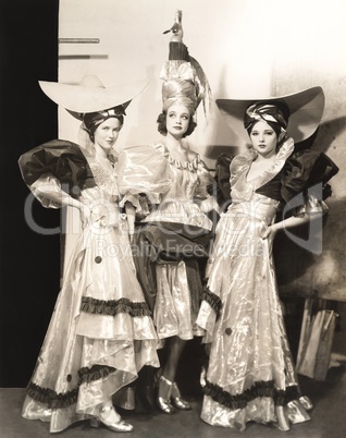 Three dancers in long dresses and large hats