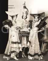 Three dancers in long dresses and large hats