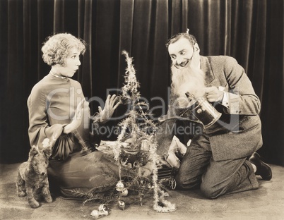 Woman watching man in fake beard watering Christmas tree